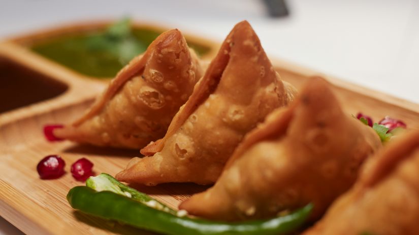 samosas kept side by side on a plate with a green chilly and pomegranate pieces next to it