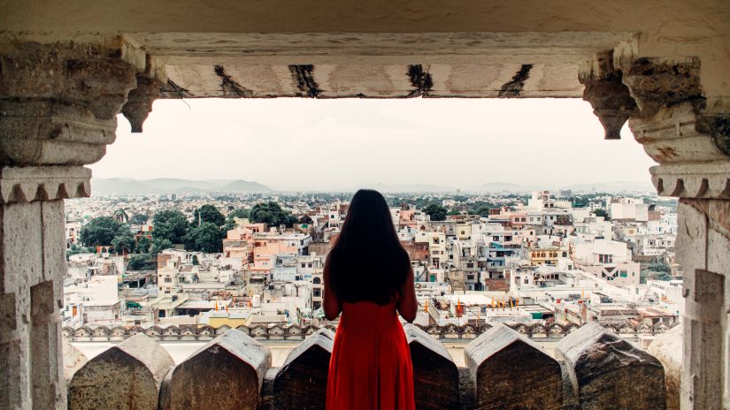 A girl looking out of a balcony of an old palace of the amazing view of the city of Udaipur- Udaipur 