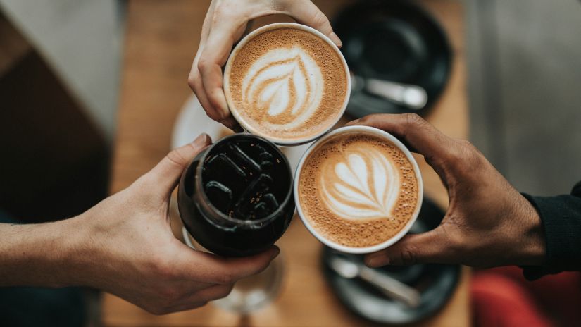 Two individuals holding cups filled with coffee, while another person holds a jar of coffee beans.