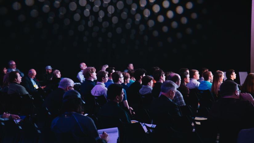 a dim-lit conference hall with people attending a symposium