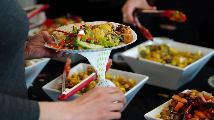 people serving themselves at a potluck that has many dishes in bowls