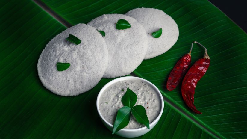 three Idlis with garnishing and coconut chutney in a bowl with chillies on the side