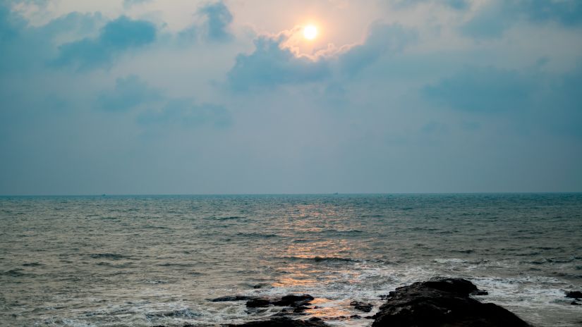 A view of anjuna beach with rocks in the foreground and the sun in the background