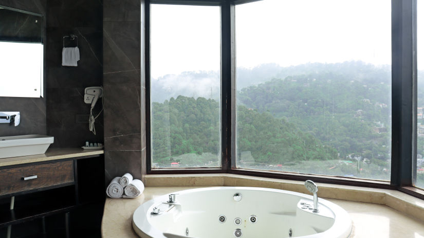 A jacuzzi in the bathroom of King Jacuzzi Suite with windows showing the valley of kasauli - Rosetum Kasauli