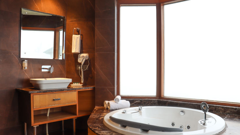 A Jacuzzi in the bathroom inside queen suite with the window having valley views - Rosetum Kasauli