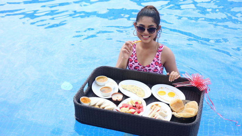 a woman posing in the swimming pool with a floating breakfast tray with many items inside - Shanti Seaview Resort & Spa