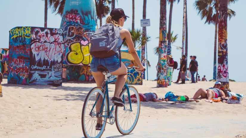 a woman cycling next to a beach on a tarred road made for bikers with palm trees in the background