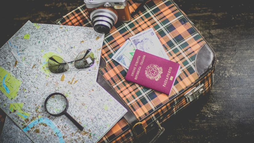 map, camera, passport, shades and a magnifying glass on a textured bag