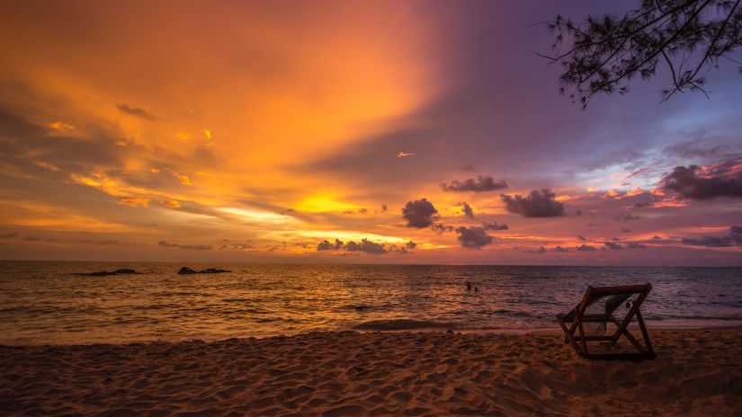 a lounge chair placed by a sea beach during sunset