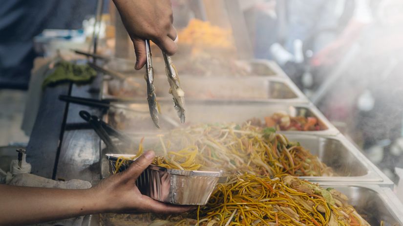 noodles being served into a bowl by a street vendor