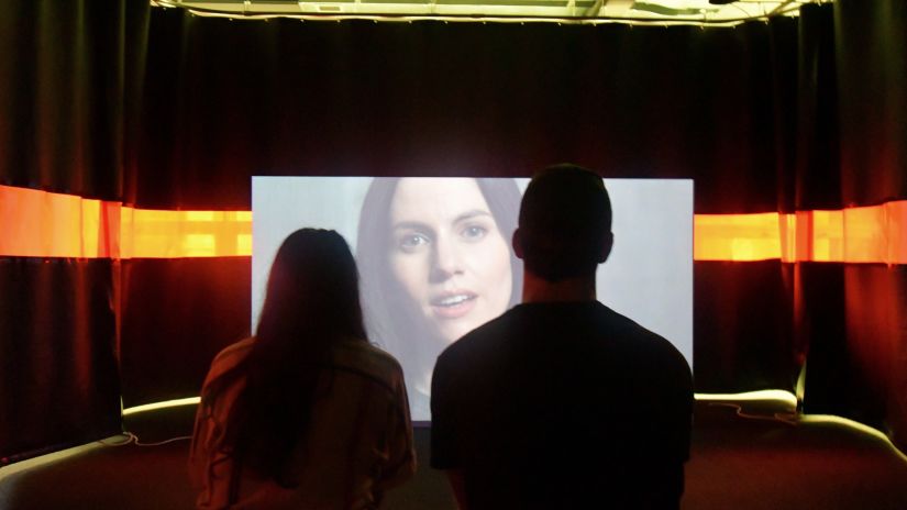 Man and a woman sitting in a dimly lit room watching media on a screen