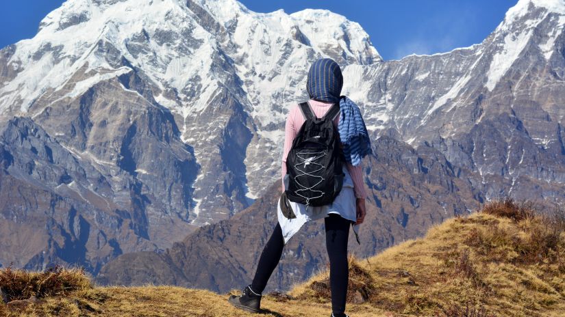 a woman looking at the snow-clad mountains standing on top of a hill