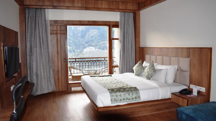 The bedroom with a double cot bed and a door leading to the balcony at The Orchid Hotel, Manali