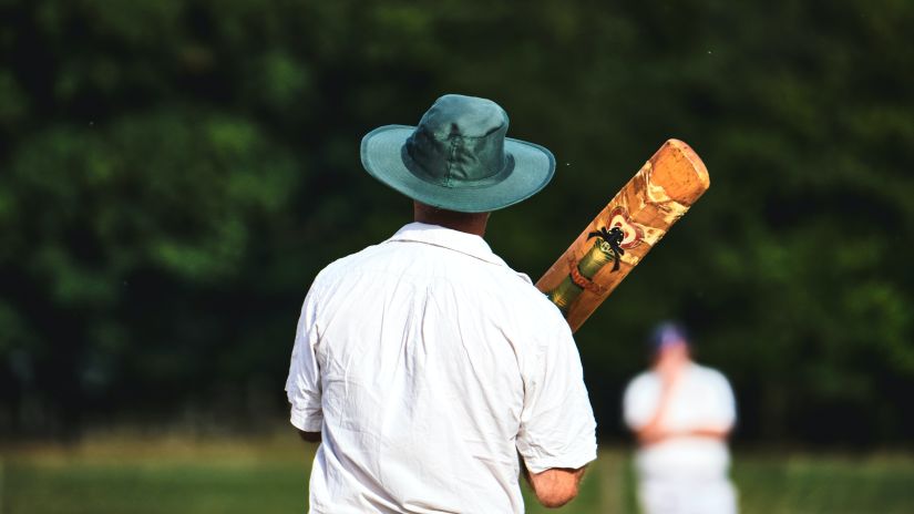 A batsman holding the bat and looking at a fielder in the background