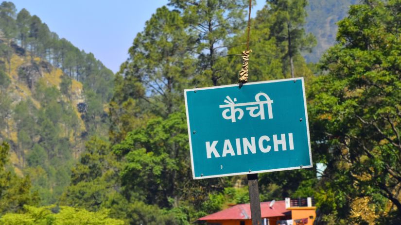 A signboard for Kainchi set amidst verdant mountains and houses