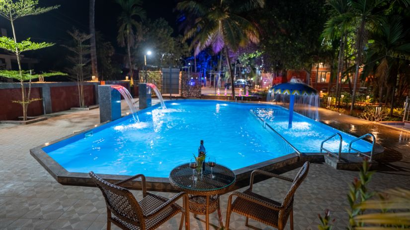 Chairs and a table in front of the swimming pool with coconut trees in the background - VITS Select Casuarina Diveagar