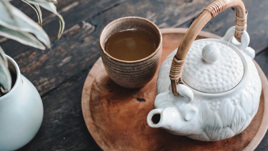 a tray with a pot and a clay cup filled with tea and a potted plant next to it