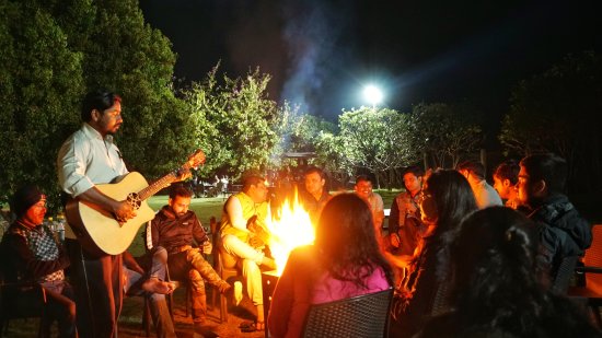 a person playing the guitar with people huddled around a campfire - The Golden tusk