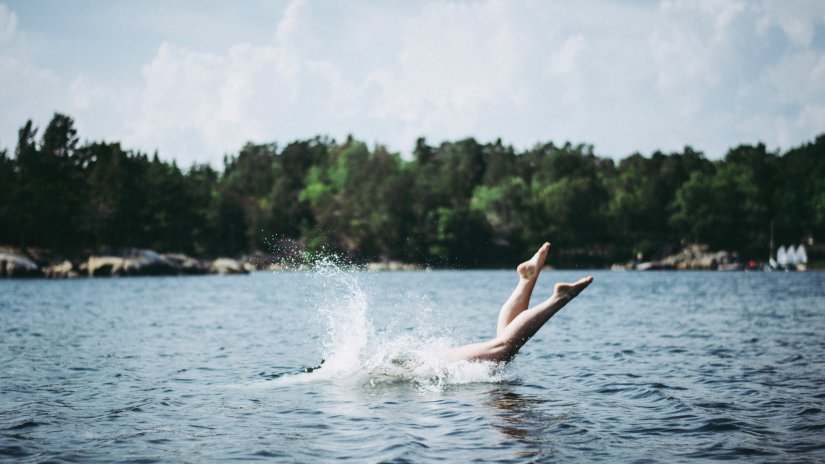 a person diving into a water body with trees in the background