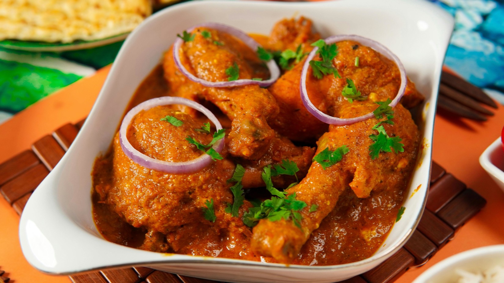 a close up shot of a chicken curry with many chicken pieces and onions kept above it