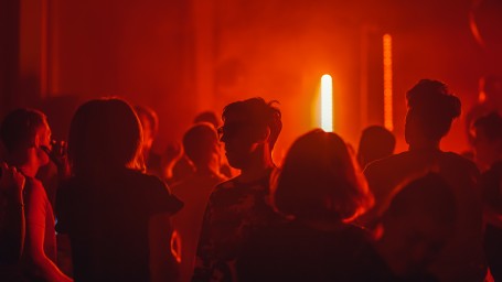 a group of people standing in a club with red neon light lighting up the room