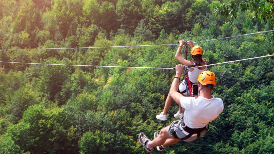 a man and a woman ziplining beside each other during daytime