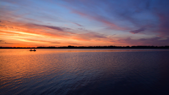 Beautiful late sunset sky over a calm lake, surrounded by a lovely landscape with trees and distant boat