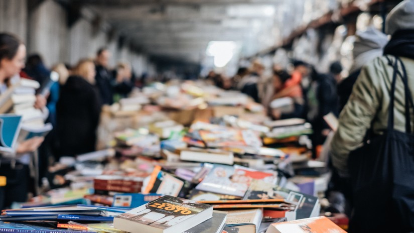 People buying books at a book fair with books in the centre and people walking on the side