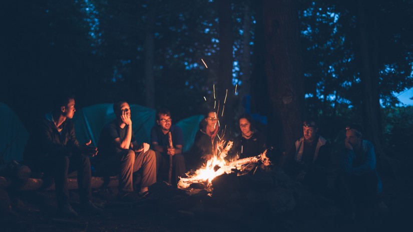 A group of people huddled around a camp fire with tents in the background