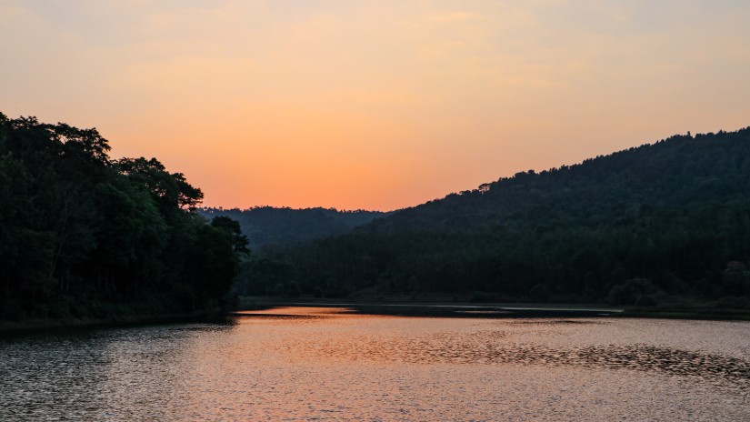 Sunset near a lake surrounded by trees and mountains