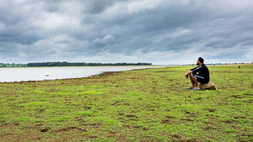 person sitting on a green field watching a river during daytime