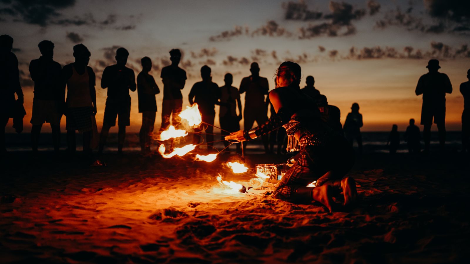 a flame dancer on a beach with onlookers at sunset