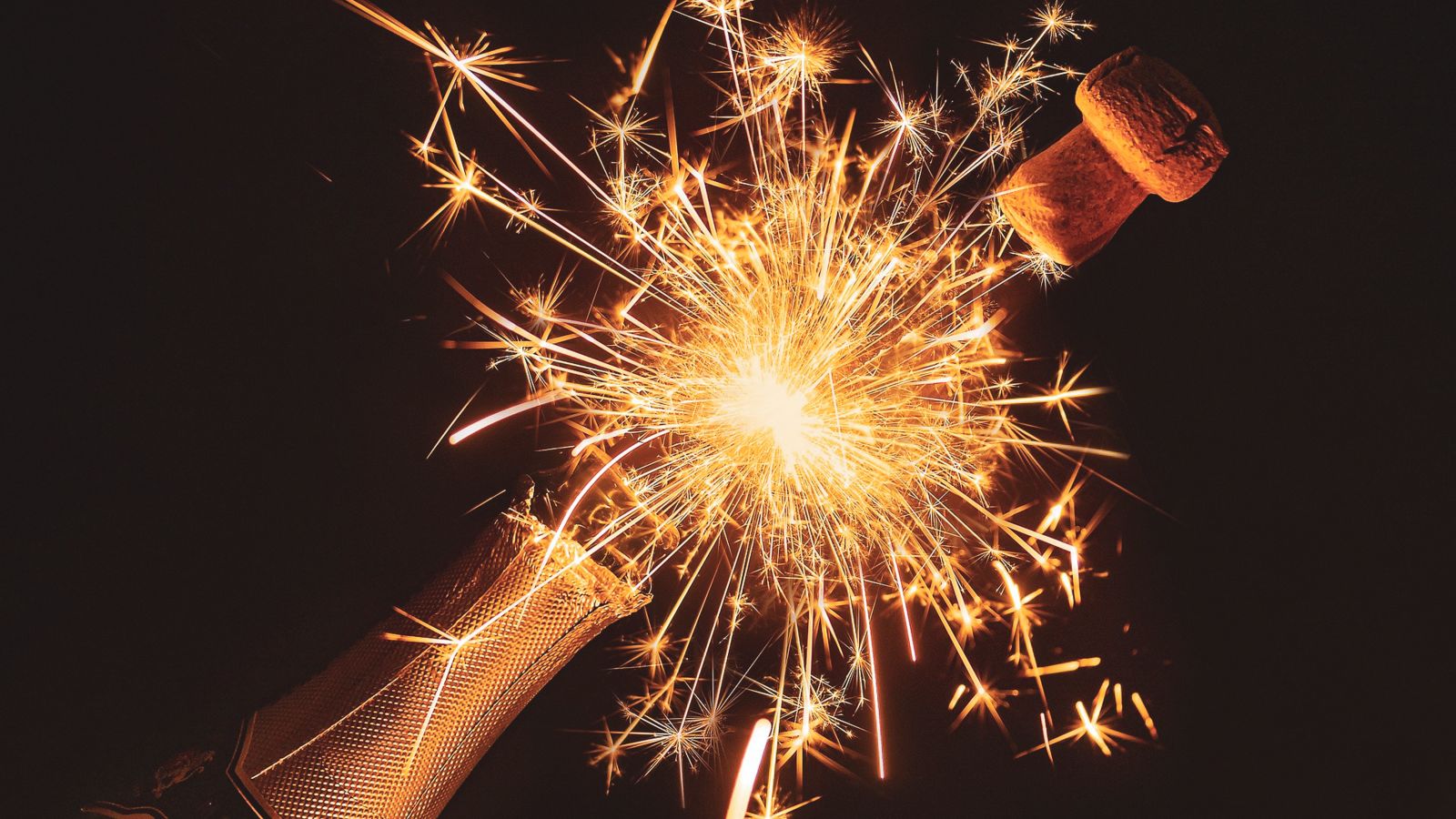 A champagne bottle popping with sparks in between the bottle's mouth and cork