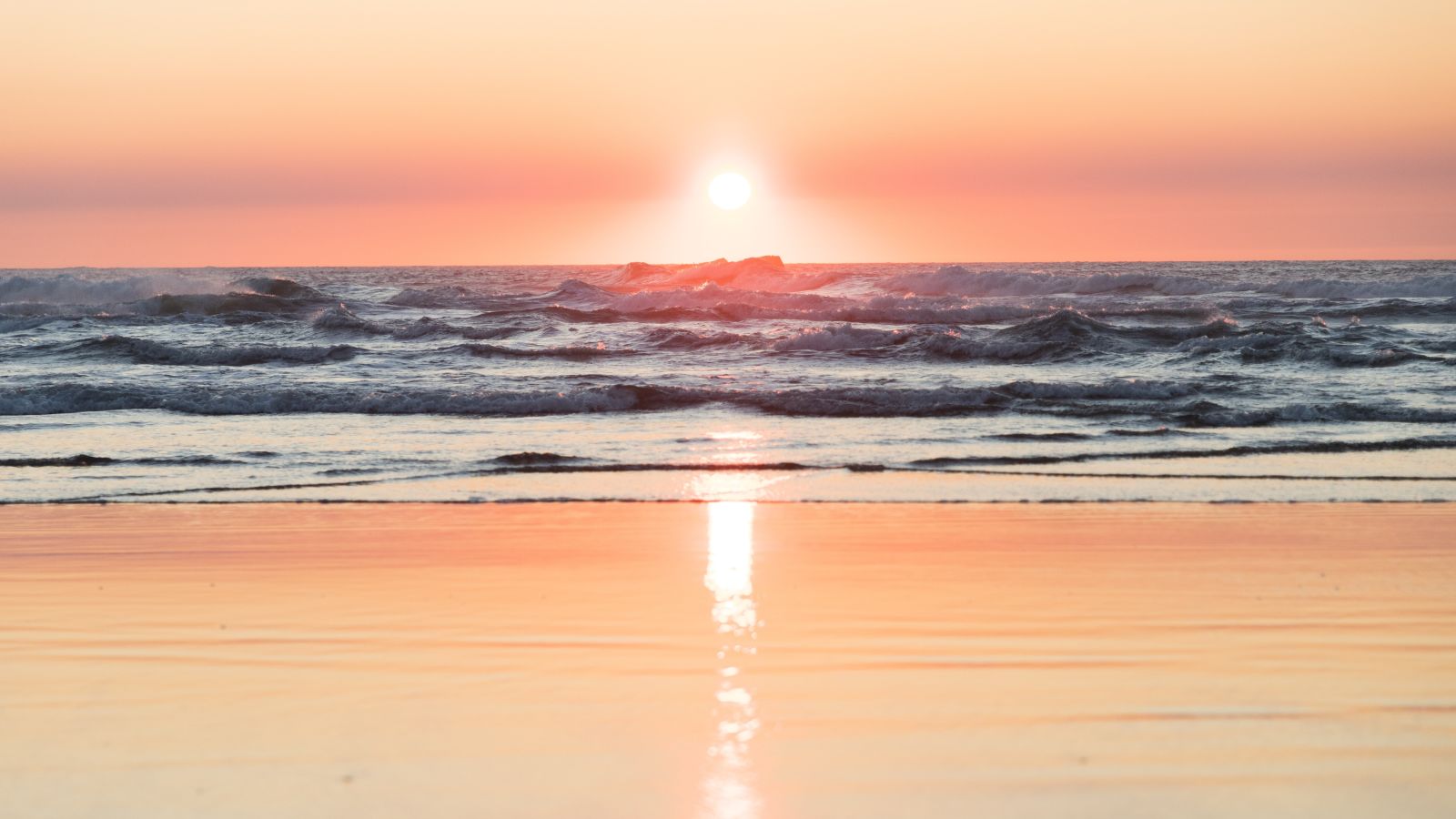 sea waves in front of the setting sun with different hues in the sky