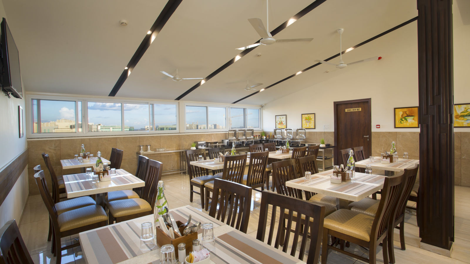 A hotel restaurant with wooden tables and chairs, large windows and ceiling fans - De Venetian by TGI, Brookefield