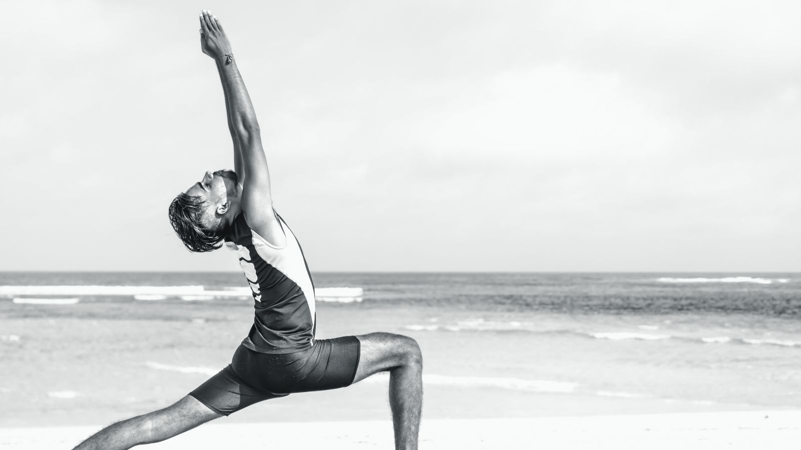 A person performing a yoga asana on the beach with the sea water overlapping the sand