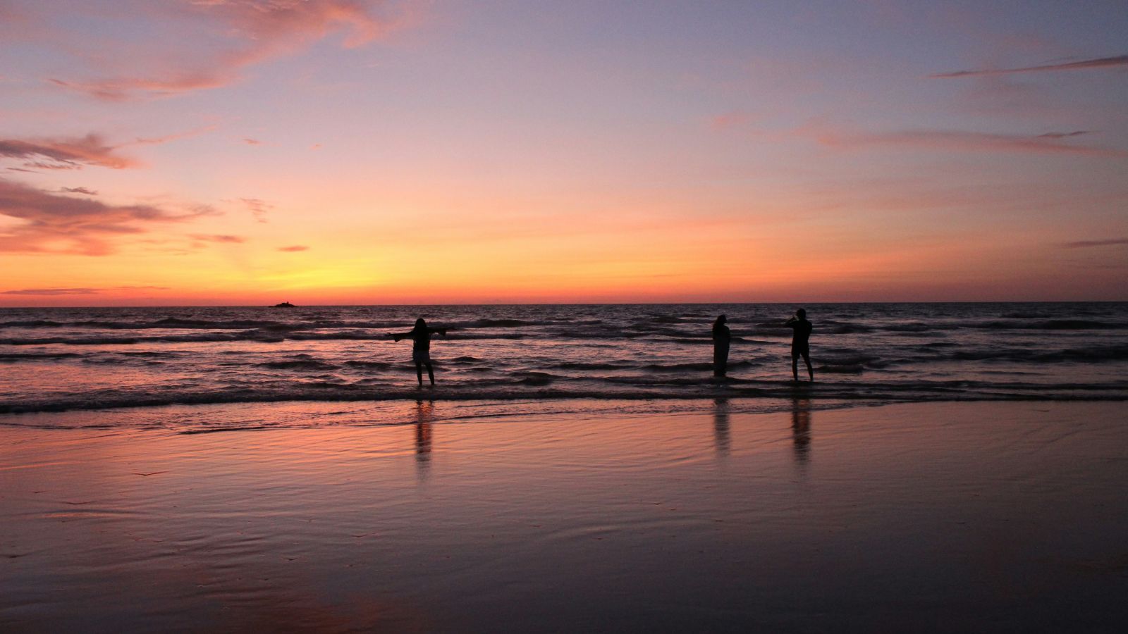a group of people walking on the beach with the sky in different hues during a sunset