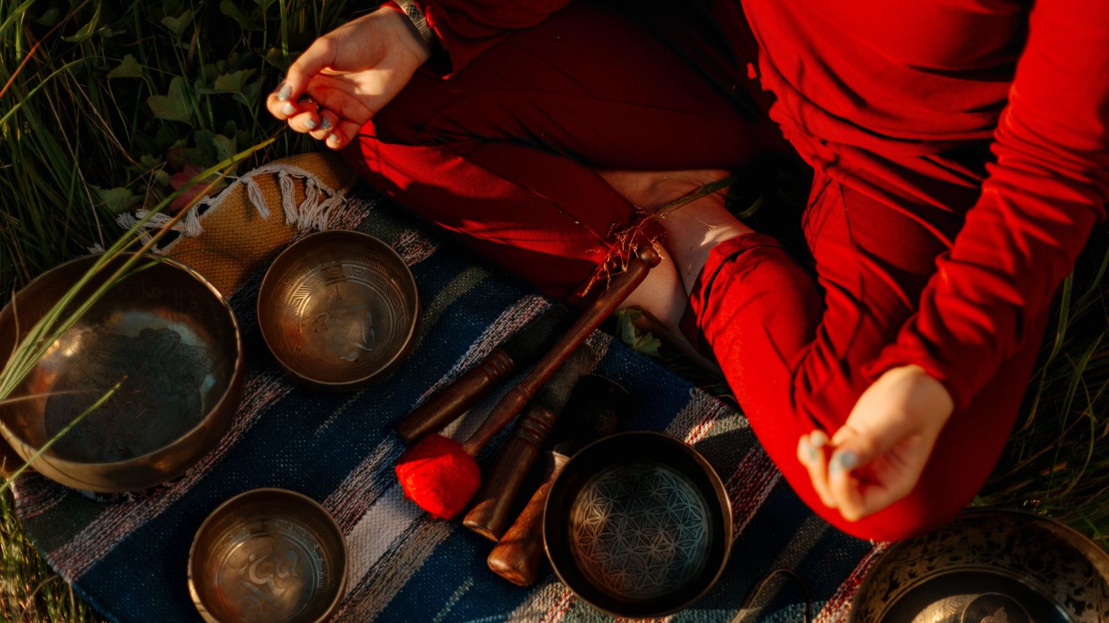 A woman sitting in a yoga pose with many bowls next to her placed on a mat for ayurveda