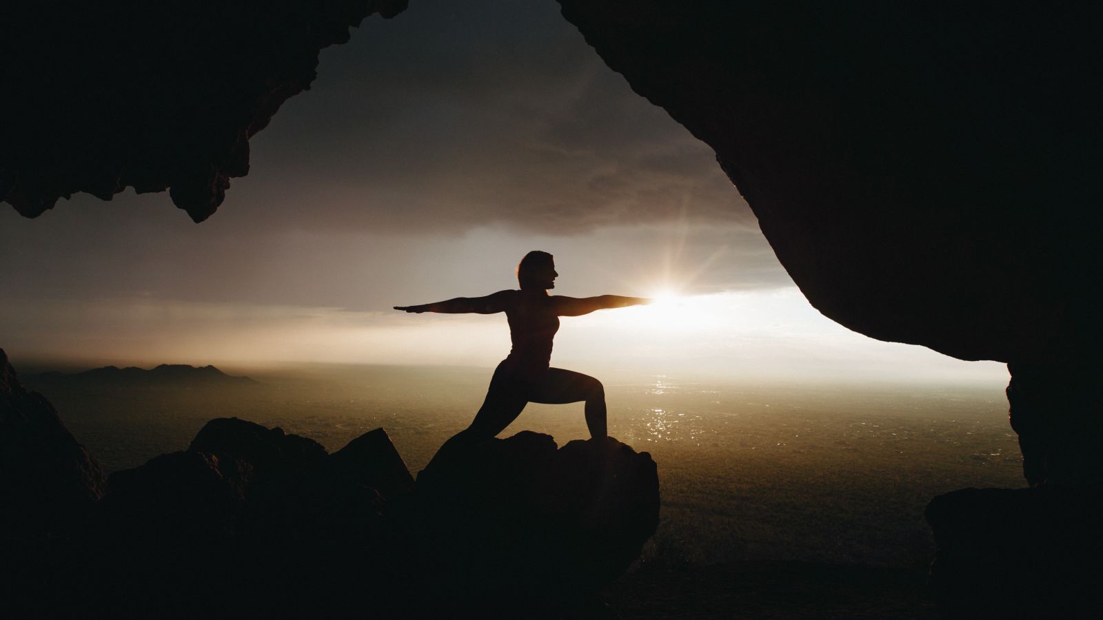 silhouette of a person doing yoga on top of a cliff during sunrise