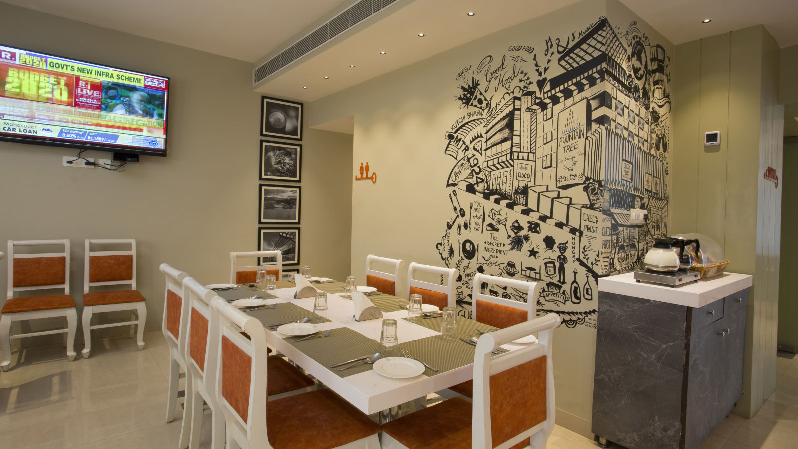 A cosy restaurant corner with a large wall mural, a buffet counter and a flat-screen TV showing news - Hotel Langford Keys by TGI, Shanti Nagar