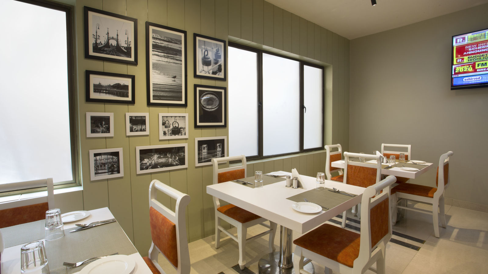 A neat dining room with white tables, orange chairs, framed black and white pictures and a TV - Hotel Langford Keys by TGI, Shanti Nagar