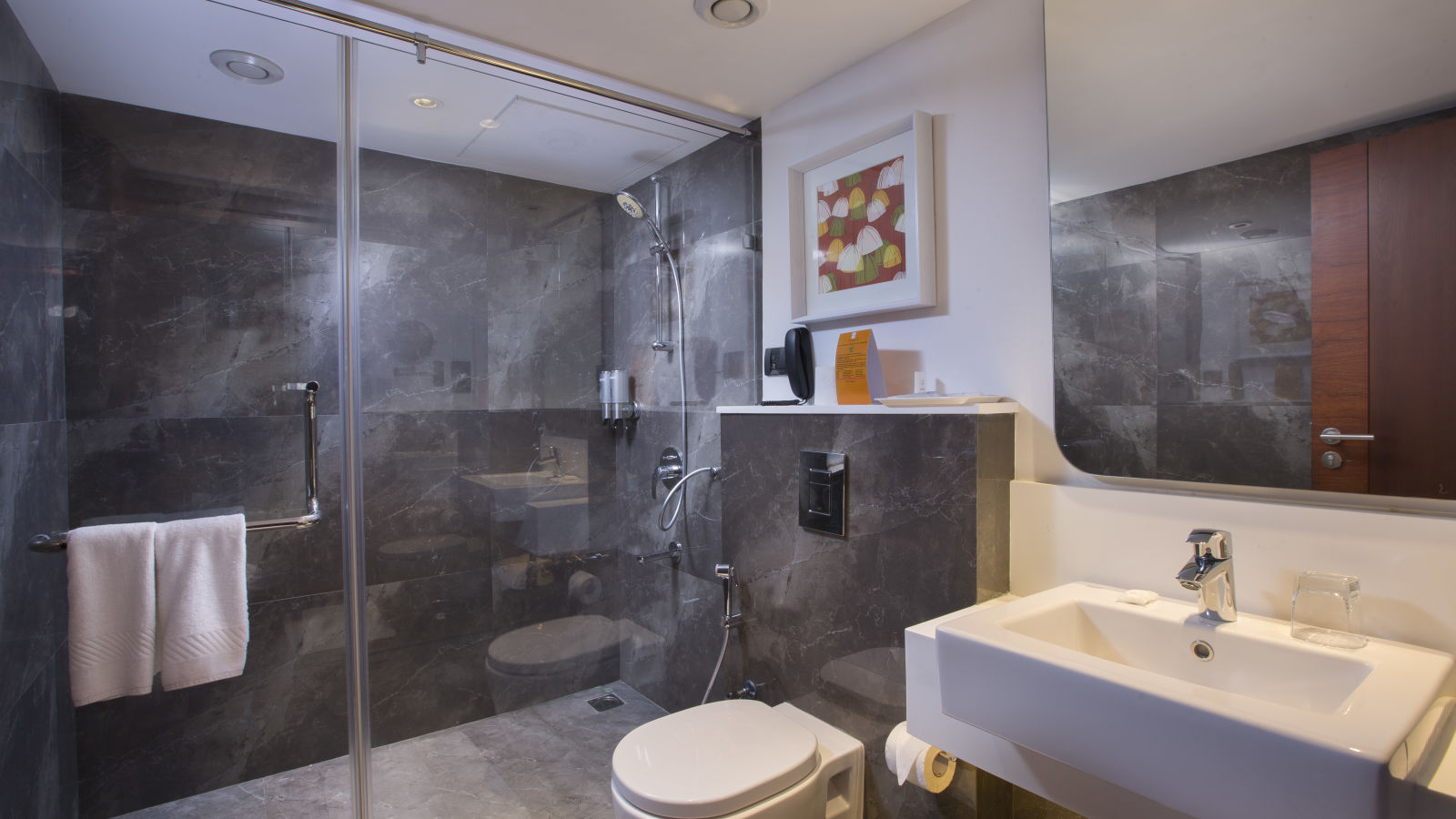 A modern bathroom with grey marble walls, a walk-in shower, white sink and a framed picture on the wall - Hotel Southend by TGI - Bommasandra, Bangalore