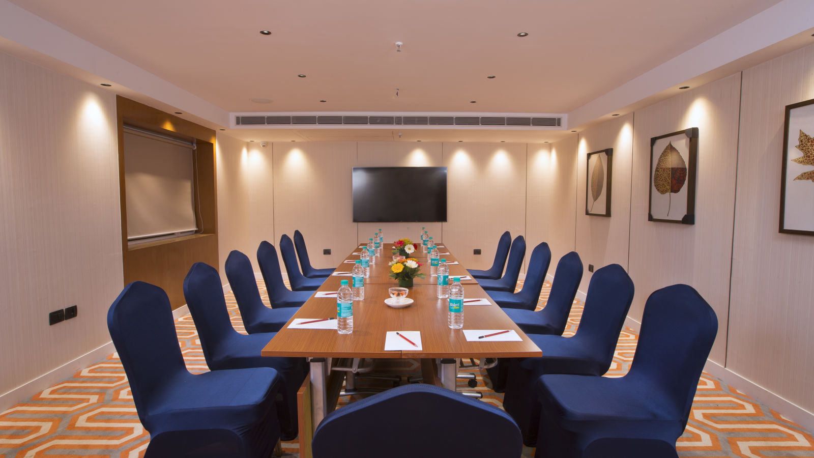 A well-lit boardroom with a long table, blue chairs and a large screen on the wall, suitable for business meetings - Hotel Southend by TGI - Bommasandra, Bangalore