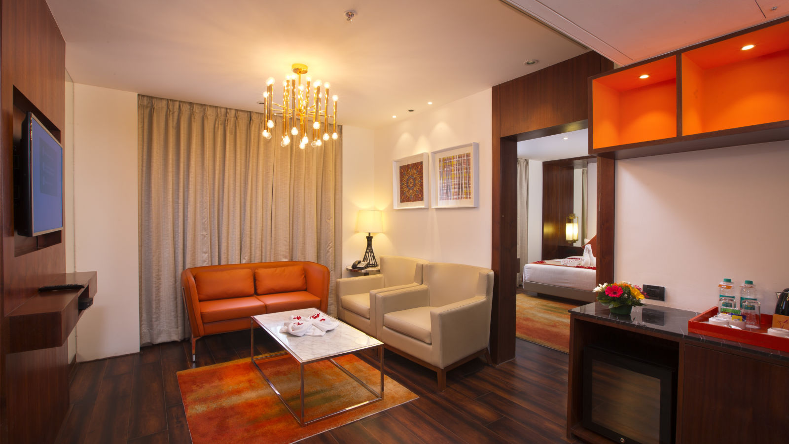 A hotel suite living area with a modern chandelier, orange leather sofa and a marble coffee table - Hotel Southend by TGI - Bommasandra, Bangalore