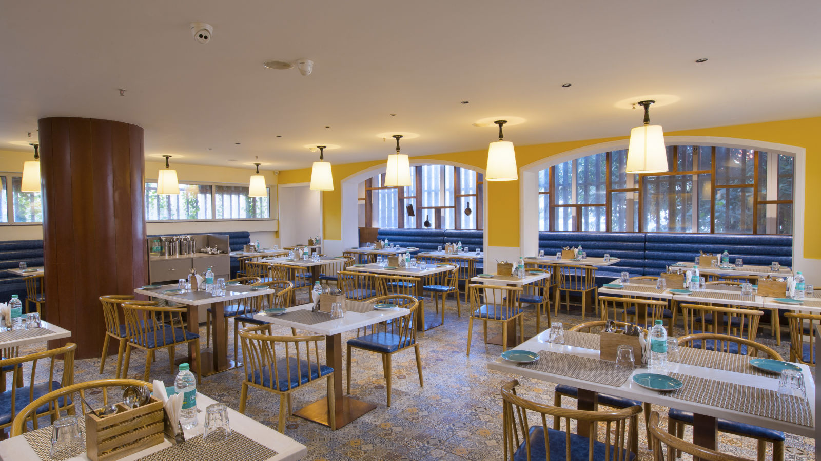 A bright and inviting restaurant interior with yellow walls, pendant lights and blue booth seating - Hotel Southend by TGI - Bommasandra, Bangalore