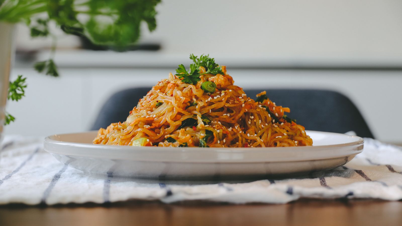 A plate consisting of Pad Thai placed on a table with a small plant in the background