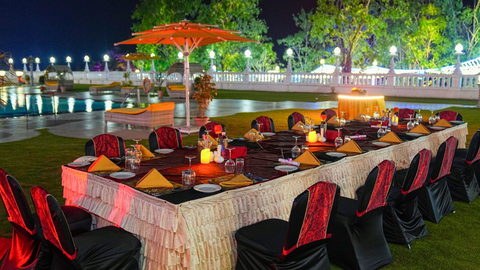 a set banquet table on a lawn with a swimming pool in the background at night