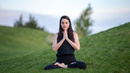 a serene image of a woman wearing black outfit meditating in the middle of green meadows