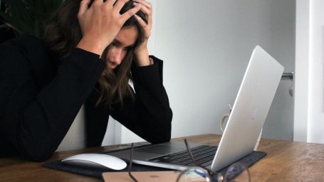 a woman holding her head looking at her laptop being stress through work