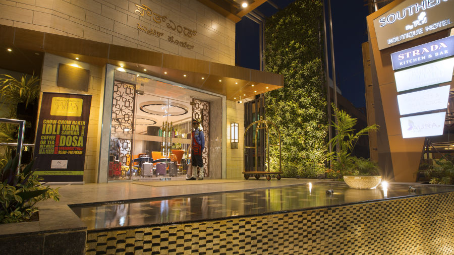 The exterior entrance of a hotel at dusk, featuring signage, a bellhop and a reflective water feature - Hotel Southend by TGI - Bommasandra, Bangalore